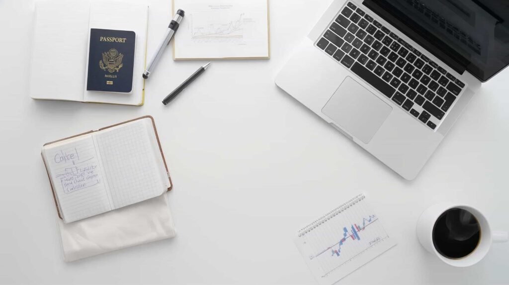 A clean, flat-lay photo of a business desk (passport, notepad, laptop, coffee cup)